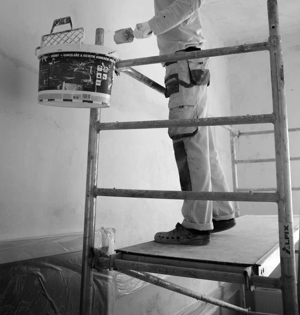 A painter on a ladder painting a white wall