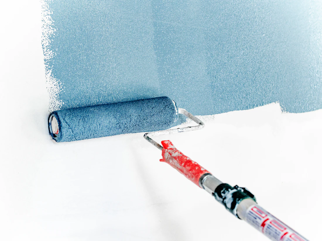 A paint roller applying blue paint to a white wall
